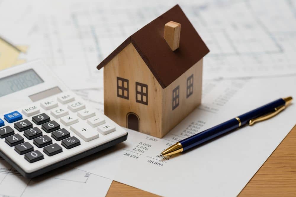 a model house sitting on construction documents next to a pen and calculator