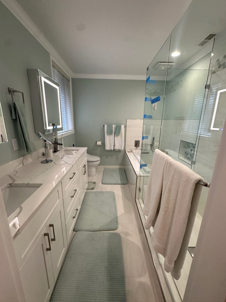 spacious and bright bathroom with white vanity, large mirrors, and a glass shower enclosure set against soft mint green walls.