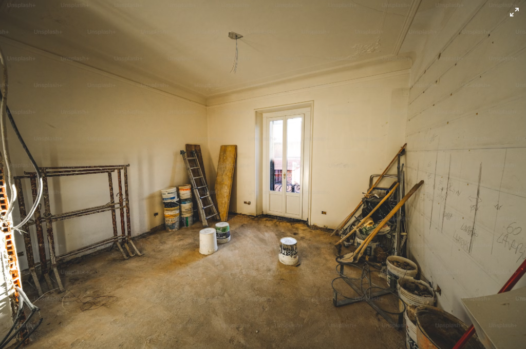 interior room under renovation with construction materials, ladders, and paint buckets scattered on the floor