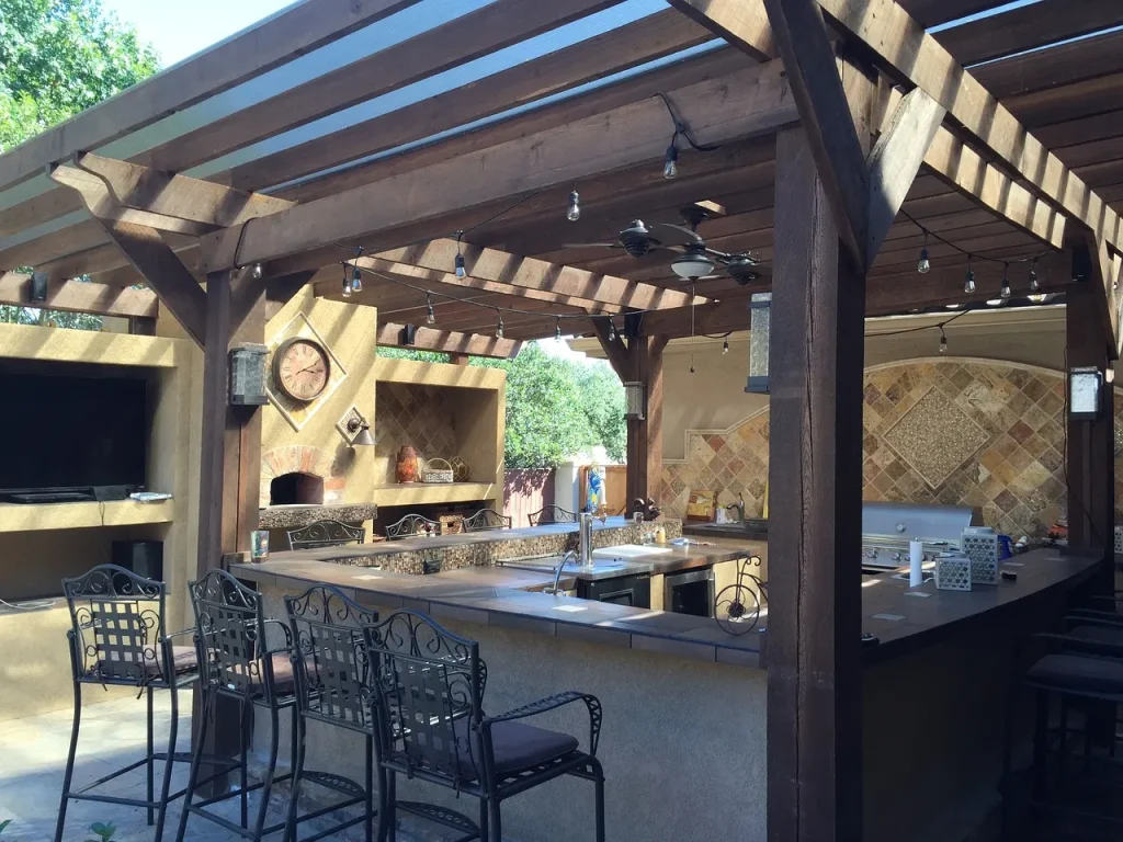 rustic outdoor kitchen and dining area under a wooden pergola by bb-builders pro.