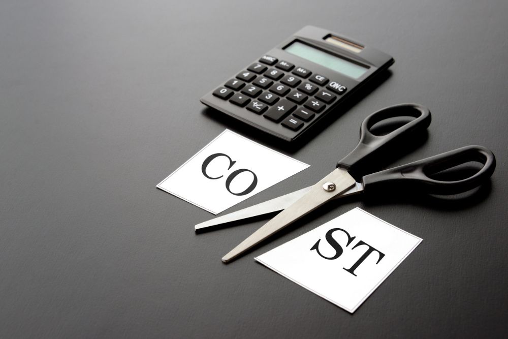 cost printed on paper symbolically cut by black scissors, next to a black calculator