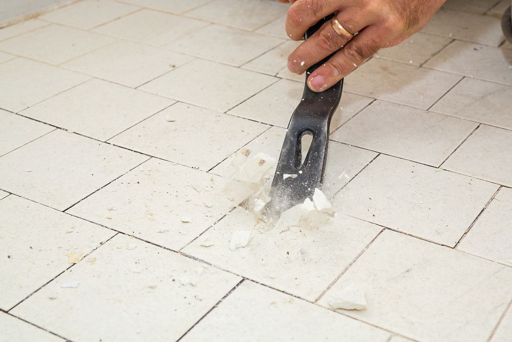 person removing bathroom tiles with a chisel-like tool
