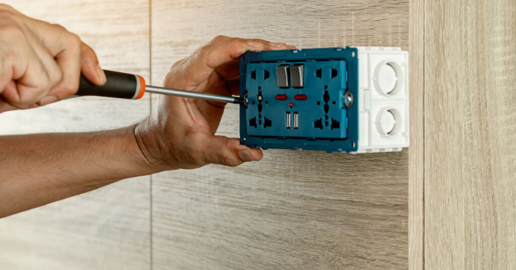 person using a screw driver to install a gfci outlet on a bathroom wall