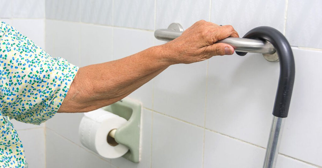 senior holding onto a grab bar with a cane hanging on it