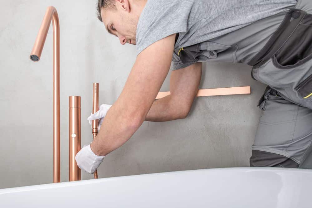 man installing the faucet, showing how to install a freestanding tub