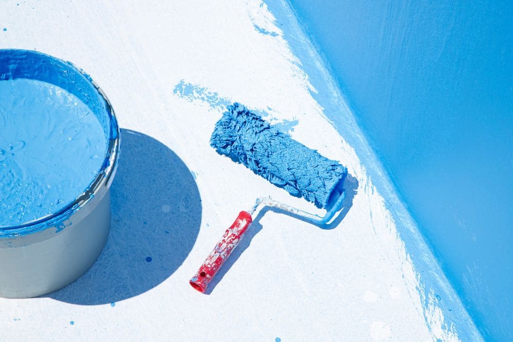 a bucket of blue waterproofing membrane and a paint roller on a half-finished waterproofed floor