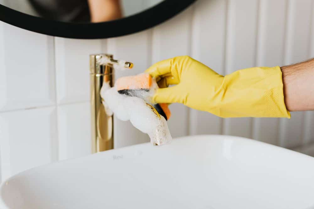 person cleaning a bathroom sink faucet