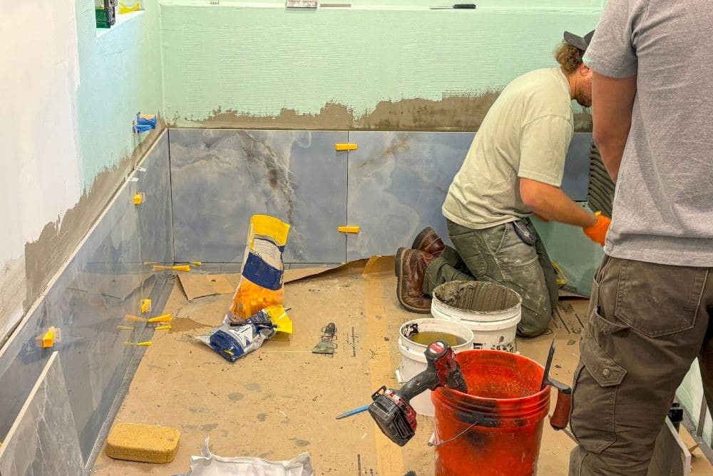 two contractors in gray shirts work together on bathroom tiles, illustrating the importance of choosing a seattle bathroom remodeling contractor based on teamwork and professional standards.