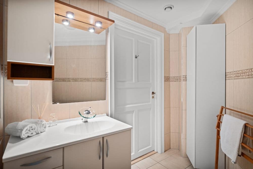 a well-lit dry area illustrating what is a hollywood bathroom, featuring a modern vanity table, a mirror framed with two focus lights, and a closed door leading to the separate shower room.