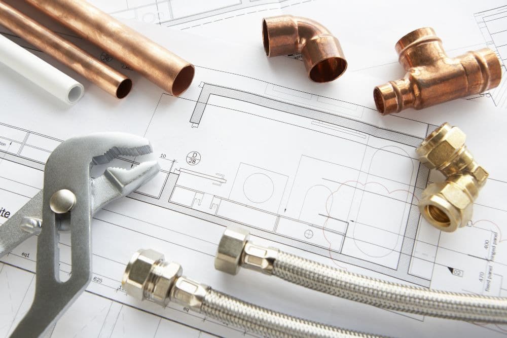 a detailed architectural drawing of a bathroom plan laid out on a table, showcasing the bathroom remodeling process seattle homeowners use to visualize layouts. a metal adjustable wrench and various brass plumbing components sit on top of the blueprint, acting as decorative paperweights.