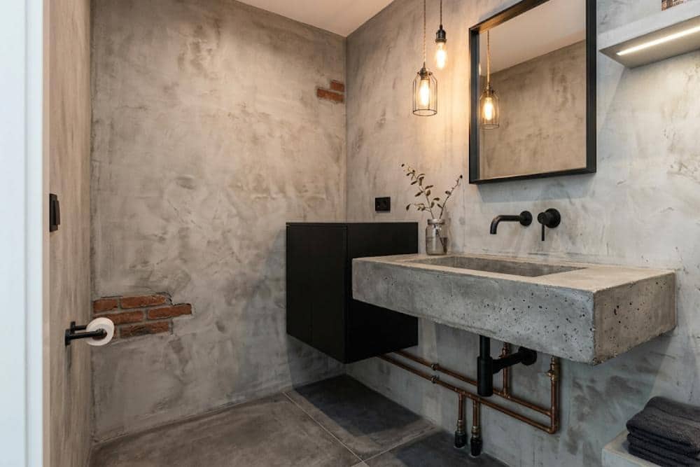 a powder room remodeled to look like an industrial loft, complete with a concrete sink, concrete-finished walls with decorative exposed red bricks, and matte black furnishings.