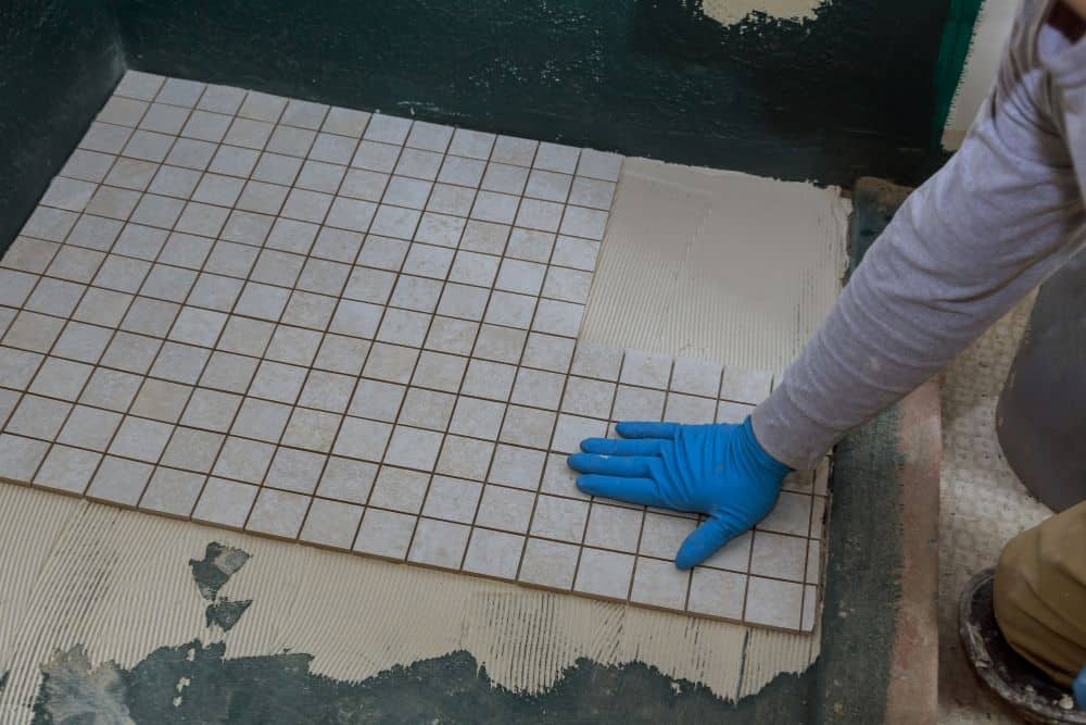a contractor installing a tile over the newly installed radiant bathroom floor heating; labor is one of the primary drivers of heated bathroom floor cost