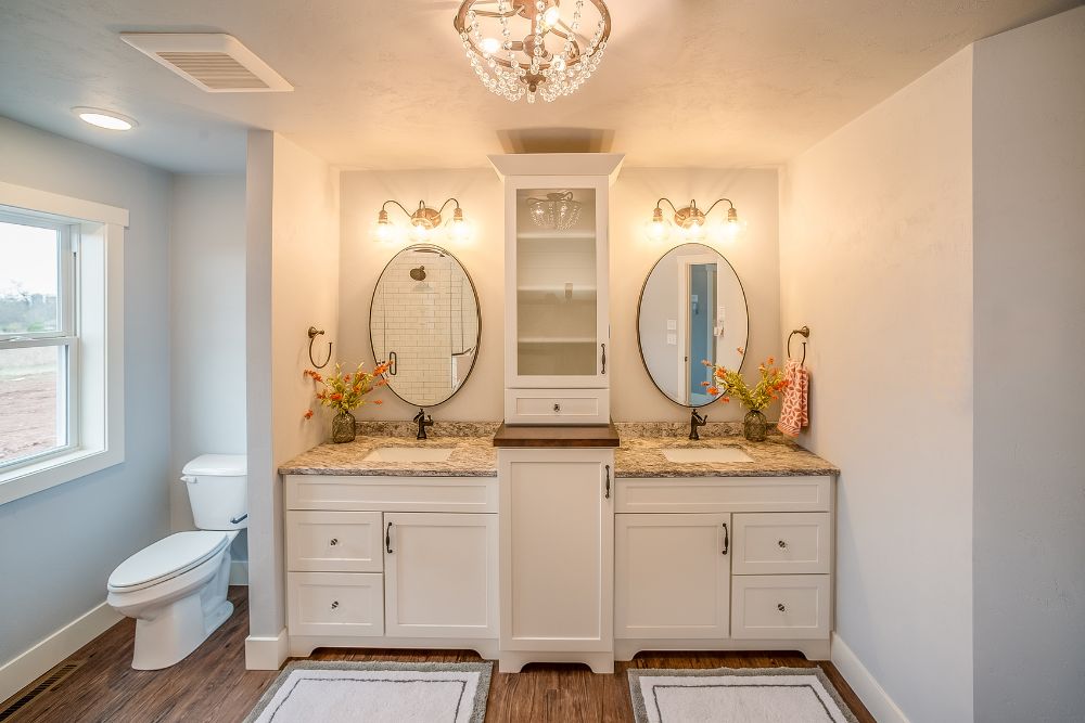 a double vanity with a vertical, custom bathroom vanity storage in between the two elliptical mirrors.